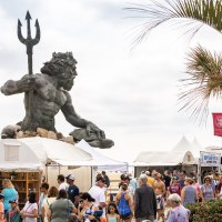 The boardwalk Neptune statute behind local business display tents with festival participants browsing the displays and walking in the foreground
